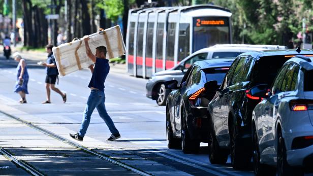 Ein Mann geht über die Straße, Autos warten, im Hintergrund fährt eine Straßenbahn.