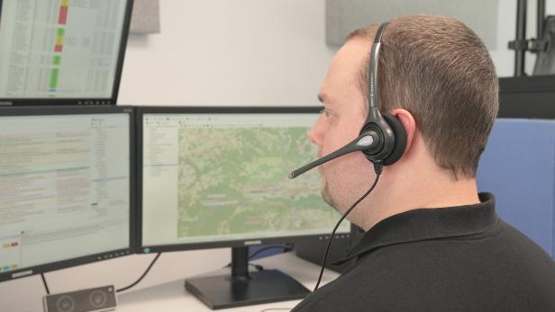 Ein Mann mit Headset sitzt vor mehreren Monitoren mit Karten- und Tabellendarstellungen.