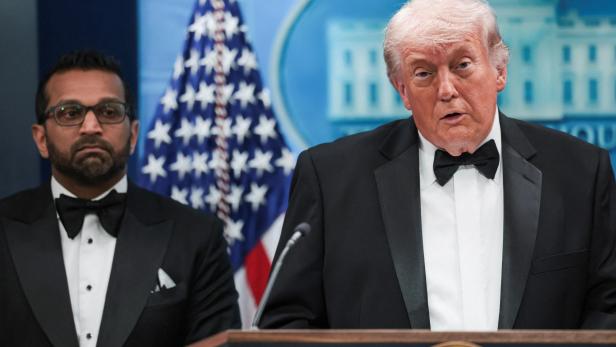 Donald Trump spricht in Anzug und Fliege vor der US-Flagge.