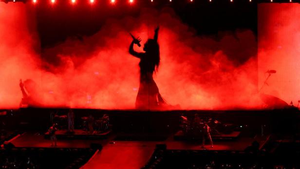 Eine Sängerin performt im roten Licht vor einem Publikum und einer Band.