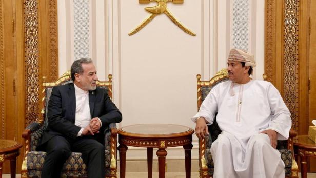 Zwei Männer sitzen in verzierten Sesseln unter dem Wappen des Oman und sprechen miteinander.