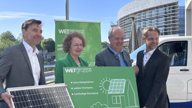 Vier Personen präsentieren ein Solarmodul und ein Schild der WET Gruppe vor einem Gebäude.