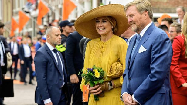 König Willem-Alexander und Königin Máxima lächeln inmitten einer Menschenmenge mit orangefarbenen Flaggen.