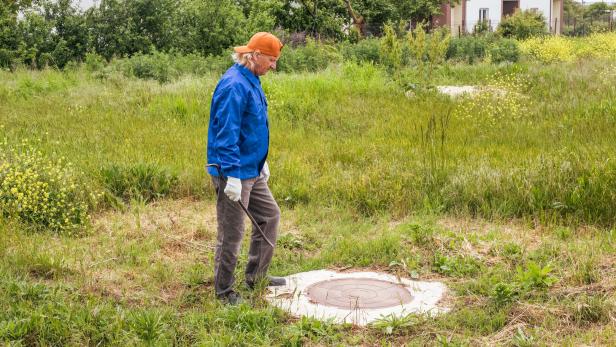 Ein Handwerker  steht vor dem Kanaldeckel auf einer Liegenschaft 