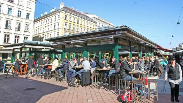 Menschen sitzen an Tischen im Freien auf dem Naschmarkt in Wien.