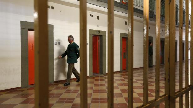 Ein Justizvollzugsbeamter geht in einem Gefängnisflur entlang, gesehen durch Gitterstäbe.
