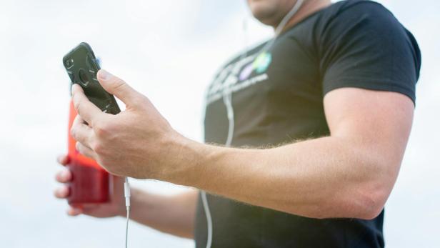 Eine Person hält ein Handy und eine Wasserflasche beim Workout