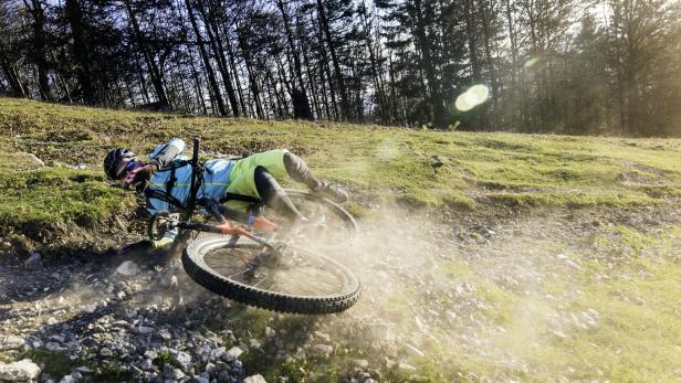 Ein Mountainbiker stürzt auf einem steinigen Weg im Gelände, Staub wirbelt auf.