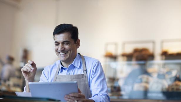 Ein lächelnder Mann mit Schürze bedient ein Tablet in einer Bäckerei.
