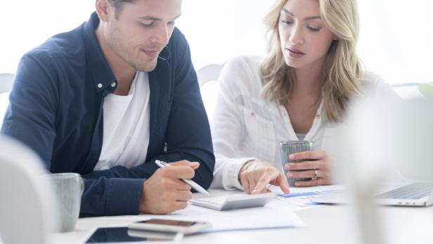 Ein Paar sitzt am Tisch, rechnet mit Taschenrechner und Stift und betrachtet Diagramme.