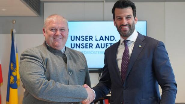 Zwei Männer schütteln sich vor einem Bildschirm mit der Aufschrift "Unser Land. Unser Auftrag.".