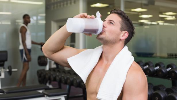 Ein Sportler trinkt ein Protein-Getränk in einem Fitnessstudio. 