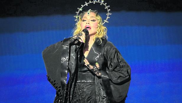 Madonna singt mit Heiligenschein und schwarzem Kimono vor blauem Hintergrund.