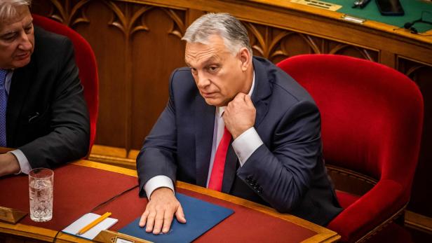 Viktor Orbán sitzt am Tisch, den Kopf in die Hand gestützt, neben ihm ein weiterer Mann im Anzug.