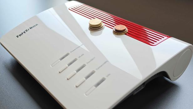 Mehrere Münzen liegen auf einem weißen Router mit roten Lüftungsschlitzen.