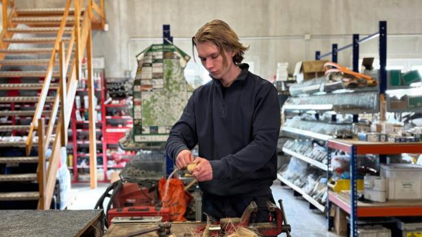 Ein junger Mann arbeitet an einer Werkbank in einer Werkstatt und hält Hanffasern in den Händen.