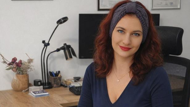 Eine Frau mit einem Haarband sitzt vor einem Computer und schaut lächelnd in die Kamera.