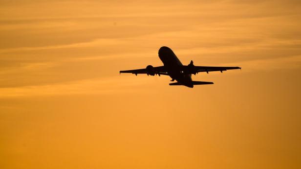 Ein Flugzeug hebt vor orangefarbenem Himmel bei Sonnenuntergang ab.