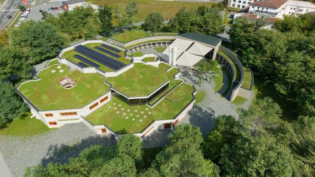 Gebäude mit begrüntem Dach, Solarpaneelen und moderner, geometrischer Architektur, umgeben von Bäumen und Parkplätzen.