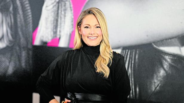 Helene Fischer lächelt in einem schwarzen Kleid mit Gürtel vor einem Hintergrund.