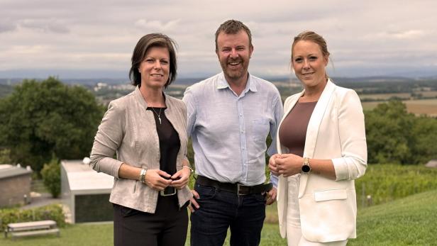 Drei Personen stehen auf einer Wiese mit Blick auf eine ländliche Landschaft im Hintergrund.