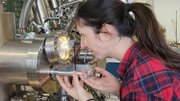 Frau betrachtet ein Experiment durch ein großes Metallgerät im Labor.