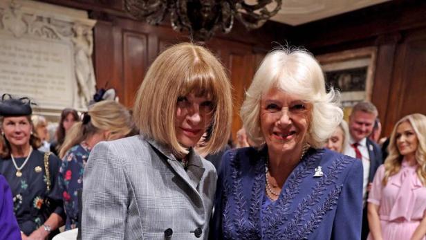 Anna Wintour und Königin Camilla stehen nebeneinander in einem festlichen Raum mit weiteren Personen im Hintergrund.