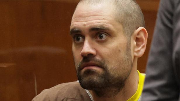 Nick Reiner mit kurzem Haar und Bart trägt braune Kleidung und sitzt mit ernstem Gesichtsausdruck in einem Raum mit Holzvertäfelung.