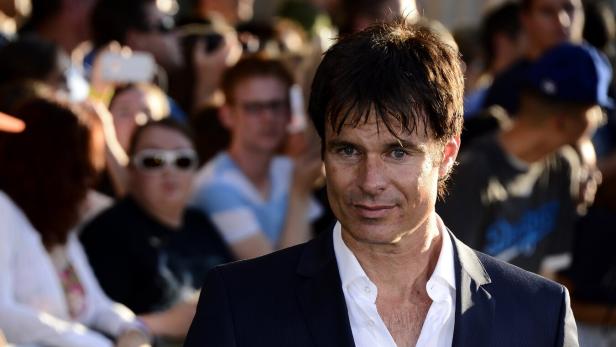 Patrick Muldoon mit dunklem Haar und offenem Hemd trägt einen dunklen Anzug vor einer Menschenmenge.