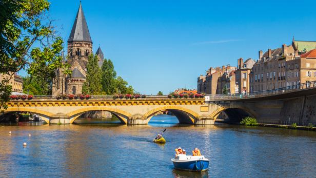 Cityscape of Metz with Temple Neuf (new temple), Moyen Bridge and Moselle River with boats and kayak in Metz, France