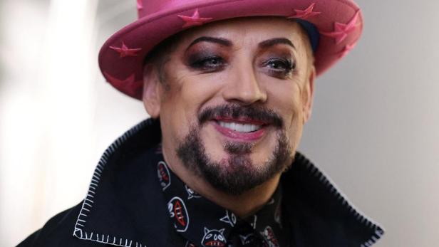 Boy George lächelt mit pinkem Hut und auffälligem Make-up.