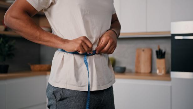 Unrecognizable sporty male sports man African guy measures waist with measuring tape check weight loss training workout sport dieting healthy nutrition control calories body muscle mass centimeters