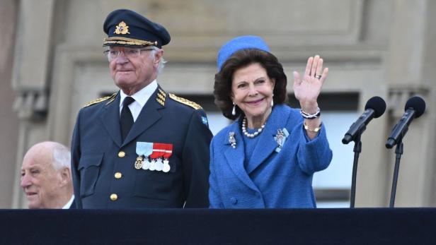 König Carl XVI. Gustaf und Königin Silvia winken von einem Balkon.