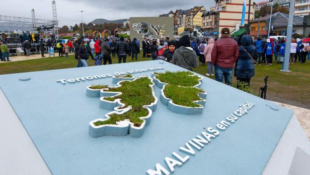 Eine Karte der Malwinen mit Grasfüllung steht auf einem Platz, umgeben von Menschen und Gebäuden.