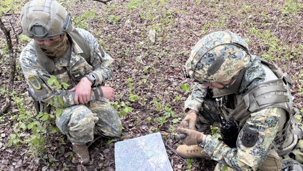 Zwei Soldaten in Tarnuniform knien im Wald und orientieren sich mit einer Karte und einem Kompass.