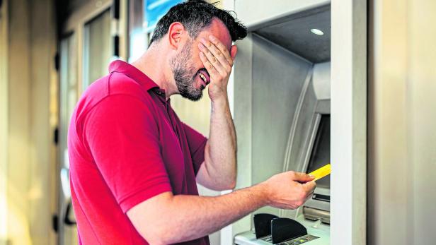 Mid-Adult Man Covering His Eyes Before Withdrawing Money Using A Credit Card At The ATM Machine