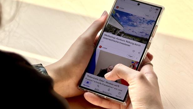 Eine Person hält ein Android-Handy und scrollt durch  Google.