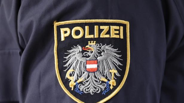 Auf dunkelblauer Uniform ist ein Abzeichen mit dem Wort „Polizei“ und einem Adler mit rot-weiß-rotem Schild zu sehen.