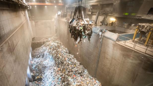 Eine Greifzange hievt Müll über einen riesigen Abfallbunker in einer Industrieanlage.