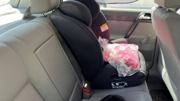 Kindersitz mit einer in Plastik verpackten Jacke auf dem Rücksitz eines Autos.