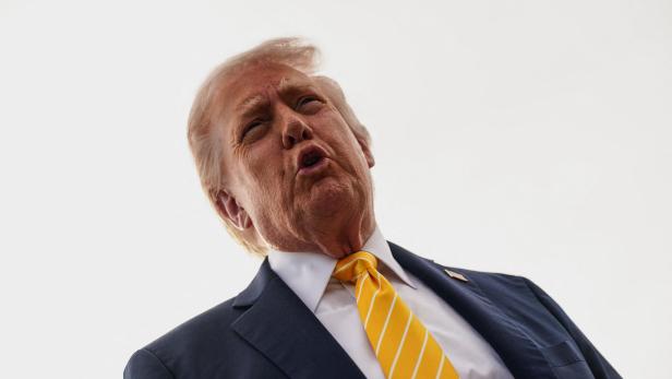Donald Trump blickt mit geöffnetem Mund nach oben, trägt einen gelb-weiß gestreiften Schlips und einen dunklen Anzug.