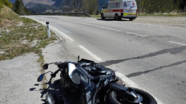Ein Motorrad liegt umgestürzt am Straßenrand, daneben ein beschädigter Helm und ein Rettungswagen steht weiter vorne.