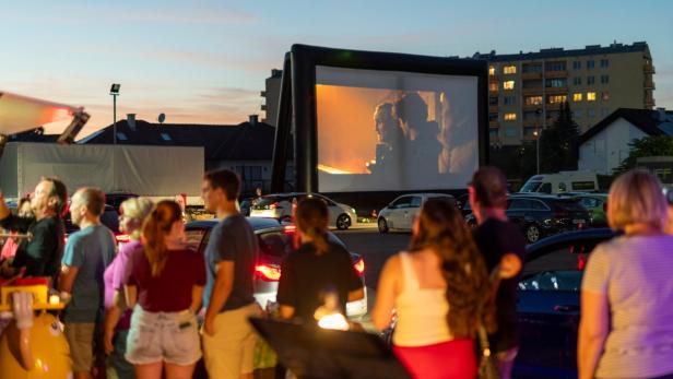 Abendliche Sommerkino-Locaton mit Publikum, Autos und Leinwand im Hintergrund
