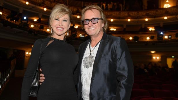 Robert Geiss mit Brille und seine Frau Carmen in Schwarz posieren in einem Theater.