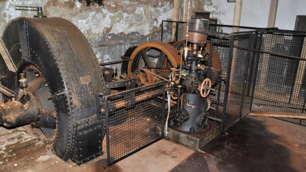 Alte, rostige Industriemaschine mit großen Schwungrädern und Schutzgitter in einem abgenutzten Raum.