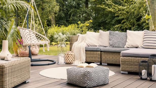 Book on a black and white pouf in the middle of a bright terrace with a rattan corner sofa, hanging chair and round rug. Real photo