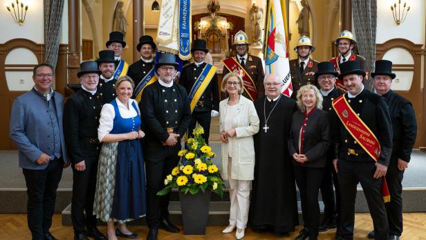 Eine Gruppe von Menschen in traditioneller und festlicher Kleidung steht in einem festlich geschmückten Raum um einen Blumenstrauß.