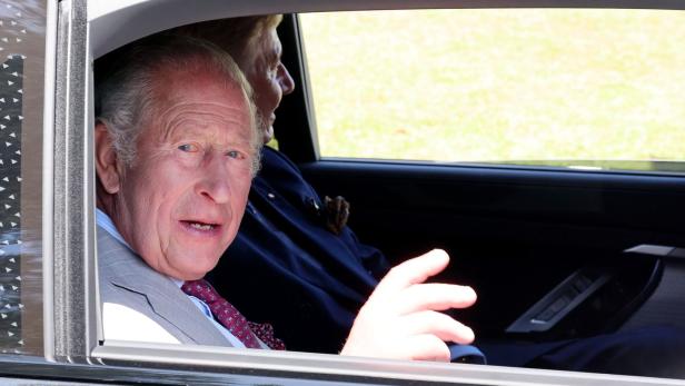 König Charles III. schaut aus dem Autofenster und gestikuliert mit der Hand.