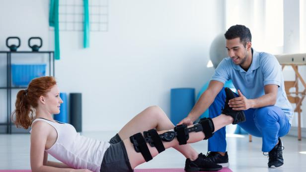 Woman with leg injury on mat and smiling doctor during treatment in the hospital
