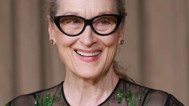 Meryl Streep lächelt mit Brille und grün verziertem Oberteil.